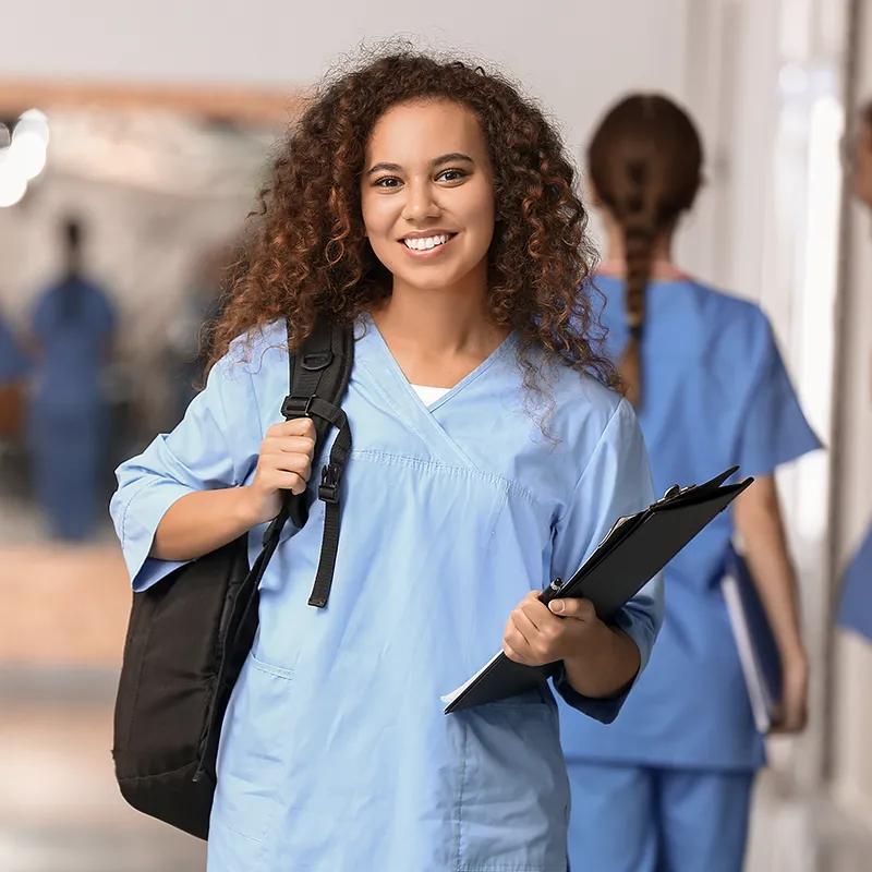 Medical student in blue scrubs standing with a backpack and clipboard