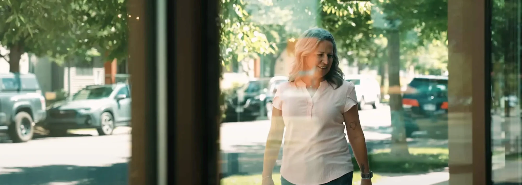 A female breast cancer survivor is walking outside. The picture is taken behind a window showing her healthy and smiling following a breast cancer diagnosis and mastectomy.