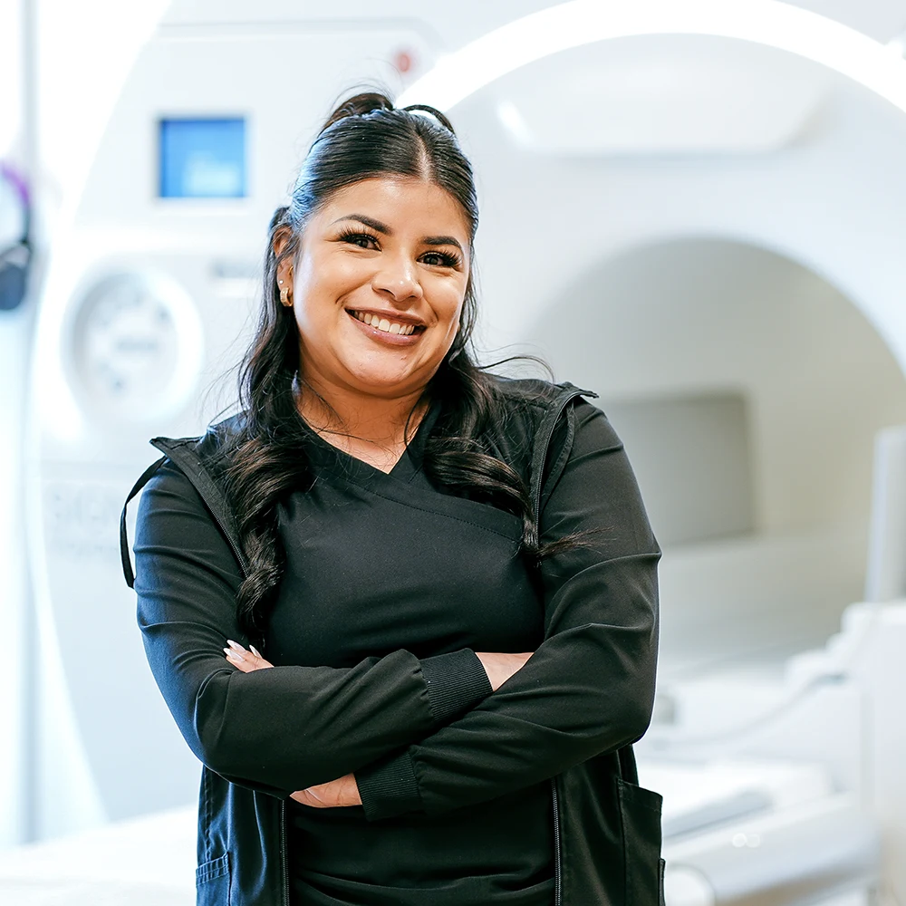 A happy Radiologist stands in front of an MRI machine.