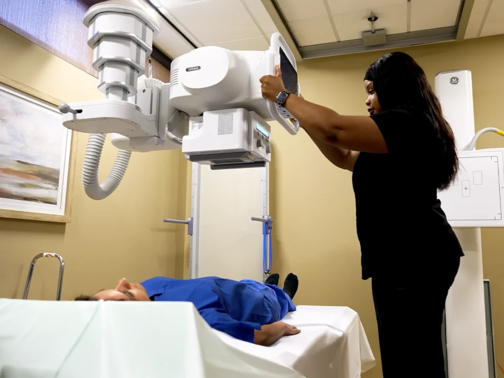 Technologist positioning X-ray equipment above a patient on an exam table